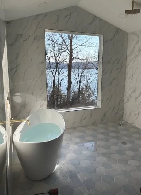 A finished bathroom remodel by Good Times Plumbing with a freestanding tub, marble tile, and a lake view